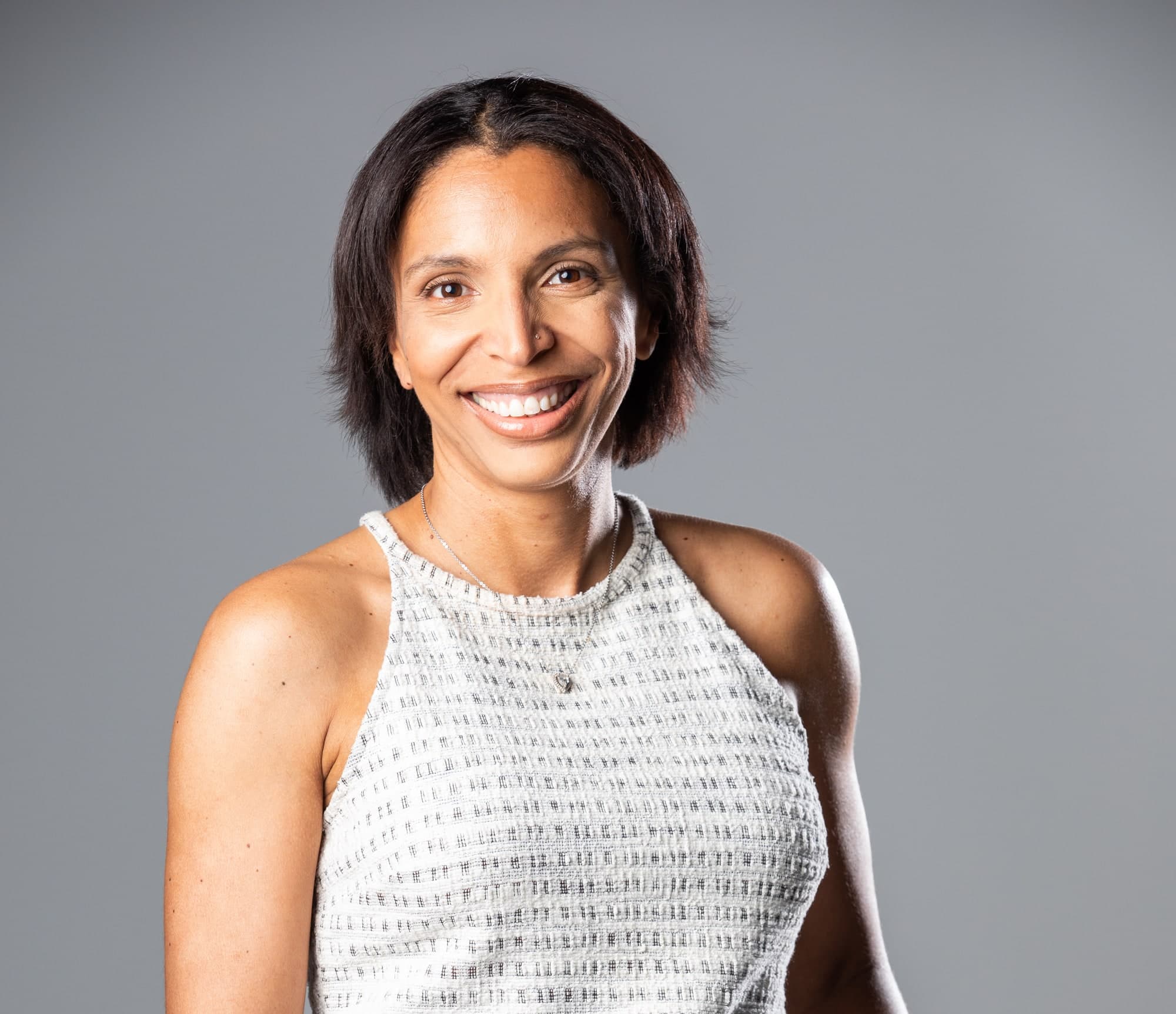 Stef, smiling, in a studio portrait against a grey background